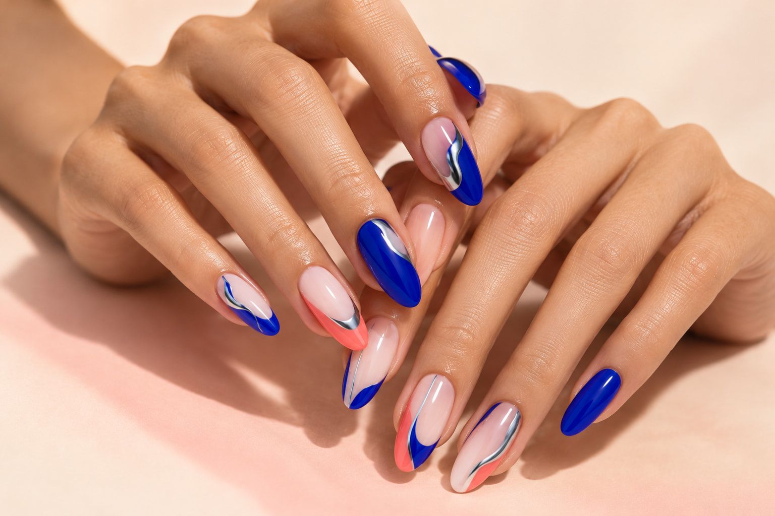 Two hands with almond nails in cobalt, coral and nude, painted with chrome-edged wave art.