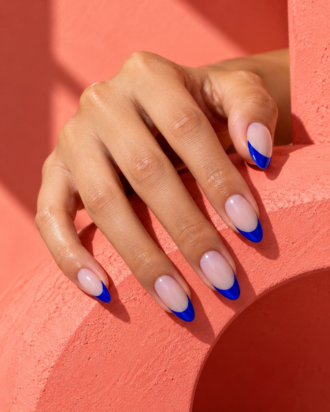 Almond nails with cobalt French tips, a hand resting on a coral block.