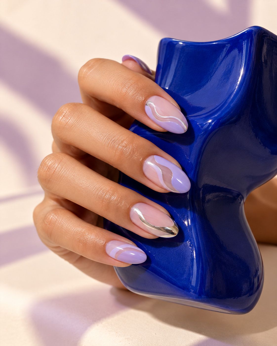 Lavender almond nails with silver chrome waves, holding a cobalt sculpture.